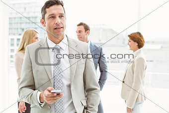 Businessman text messaging with colleagues in meeting behind