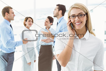 Businesswoman using mobile phone with colleagues behind
