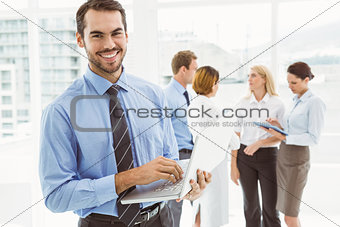 Businessman using laptop with colleagues behind