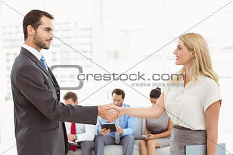 Businessman shaking hands with woman besides people waiting for interview