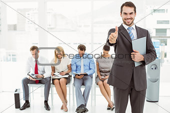 Businessman gesturing thumbs up against people waiting for interview