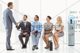 Businessman shaking hands with man besides people waiting for interview