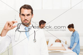 Doctor holding injection with colleagues and patient behind