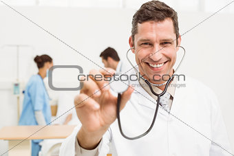 Doctor using stethoscope with colleagues and patient behind