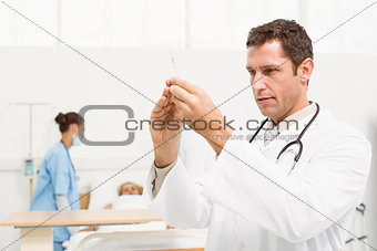 Doctor holding injection with colleagues and patient behind