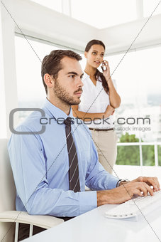 Businessman using computer while woman on call