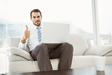 Businessman with laptop gesturing thumbs up in living room
