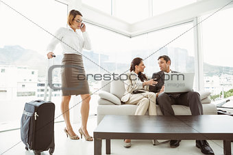 Business people using laptop and colleague with luggage