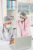 Doctors wearing surgical masks while using laptop at medical office