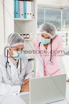 Doctors wearing surgical masks while using laptop at medical office