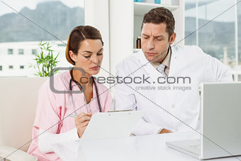 Doctors reading reports while using laptop at medical office