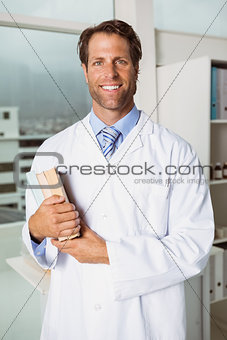 Smiling male doctor holding books in medical office