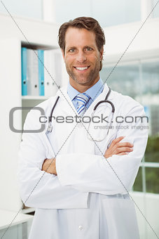 Smiling doctor with arms crossed in medical office