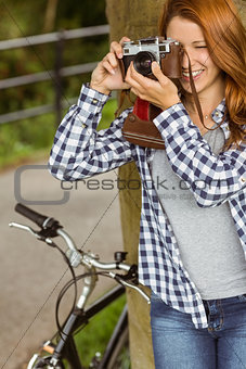 Young redhead taking a picture leaning against a tree