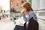 Woman drinking coffee and using laptop outside