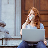 Beautiful woman drinking of disposable cup using her laptop