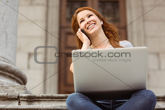 Smiling girl calling with her mobile phone and using laptop