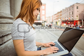 Focused pretty redhead typing on laptop