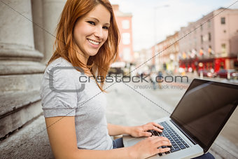 Smiling pretty redhead typing on laptop