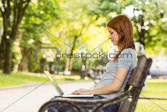 Woman sitting on park bench using laptop