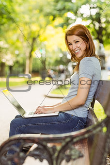 Redhead sitting on bench using laptop smiling at camera