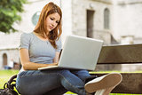 Happy girl sitting on bench using laptop