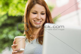 Woman with disposable cup and laptop sitting on bench