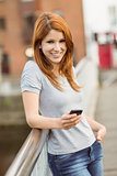 Smiling redhead with her mobile phone texting a message
