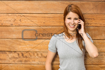Cheerful redhead leaning against wall phoning