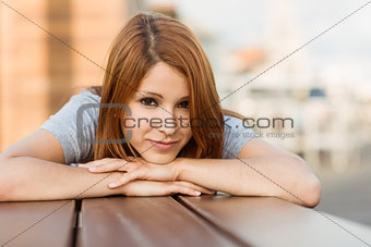 Smiling pretty redhead lying on bench on a sunny day