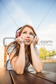 Pretty redhead lying on bench listening to music