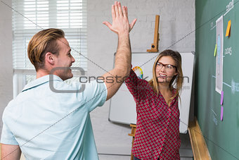 Creative business people high fiving by blackboard