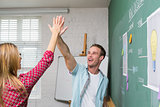 Creative business people high fiving by blackboard