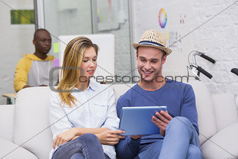 Casual colleagues using digital tablet on couch in office