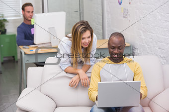 Casual colleagues using laptop on couch in office