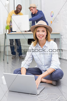 Casual woman using laptop with colleagues behind in office