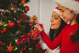 Mother and daughter hanging christmas decorations on tree