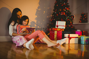 Mother and daughter using tablet beside the christmas tree