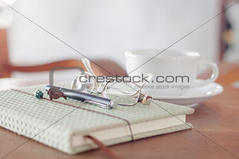 Notebook with pen, eyeglasses and white coffee cup