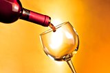 bottle of red wine beginning filling a glass on golden background