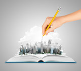 Hand drawing a city on an open book