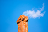 Brick chimney releasing smoke on sky.