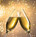 champagne flutes with golden bubbles on light bokeh background