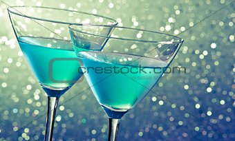 two glasses of blue cocktail on dark green tint light bokeh