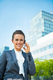 Smiling business woman talking mobile phone in front of office b