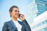 Smiling business woman talking mobile phone in front of office b