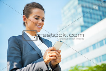 Happy business woman writing sms in front of office building