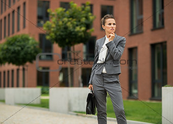 Thoughtful business woman with briefcase in front of office buil