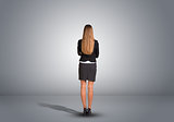 Businesswoman standing in an empty gray room. Rear view