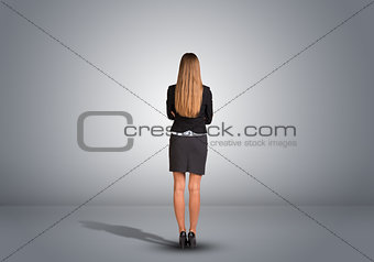 Businesswoman standing in an empty gray room. Rear view